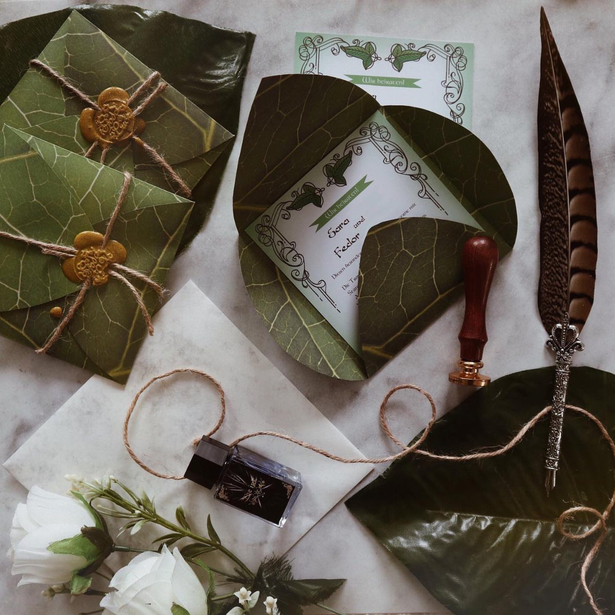 Hobbit Themed Wedding: 20 Ideas for Your Shire Celebration 4 Leaf-shaped green envelopes with gold wax seals, a quill, and an invitation on a white background.