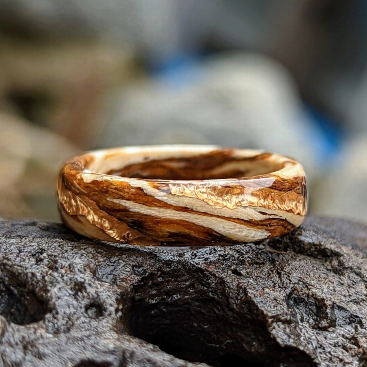Hobbit Themed Wedding: 20 Ideas for Your Shire Celebration 5 A patterned wooden wedding ring resting on a dark, textured piece of volcanic rock.