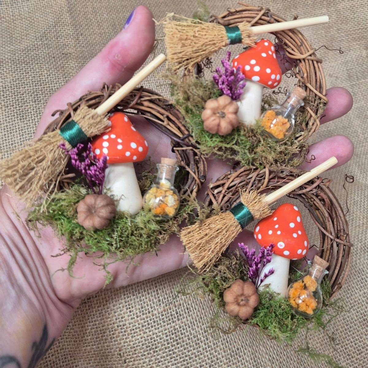 Hobbit Themed Wedding: 20 Ideas for Your Shire Celebration 20 A hand holding three small twig wreaths decorated with tiny brooms, mushrooms, and miniature pumpkins.