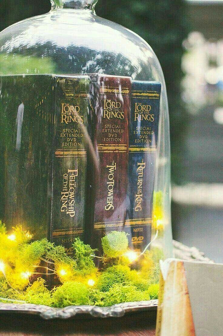 Lord of the Rings Centerpieces: 7 Tabletop Ideas for Your Event 5 Lord of the Rings DVD cases displayed inside a glass cloche with green moss and fairy lights.