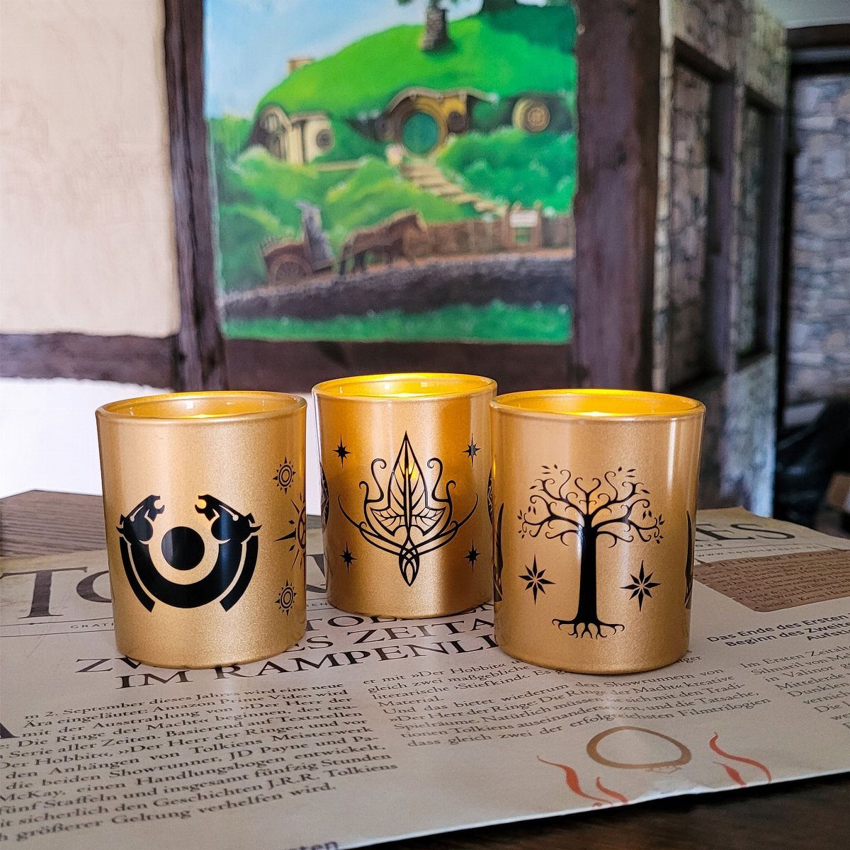 Lord of the Rings Centerpieces: 7 Tabletop Ideas for Your Event 7 Three gold frosted glass votive holders with black symbols resting on a newspaper.