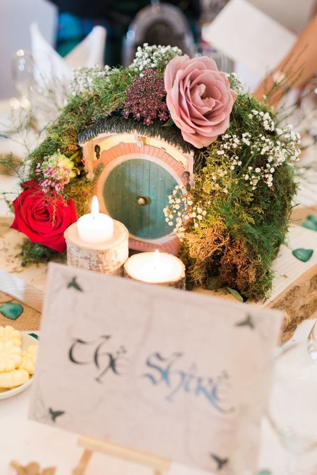 Lord of the Rings Centerpieces: 7 Tabletop Ideas for Your Event 1 Miniature hobbit cottage door surrounded by moss, roses, and lit candles on a table.