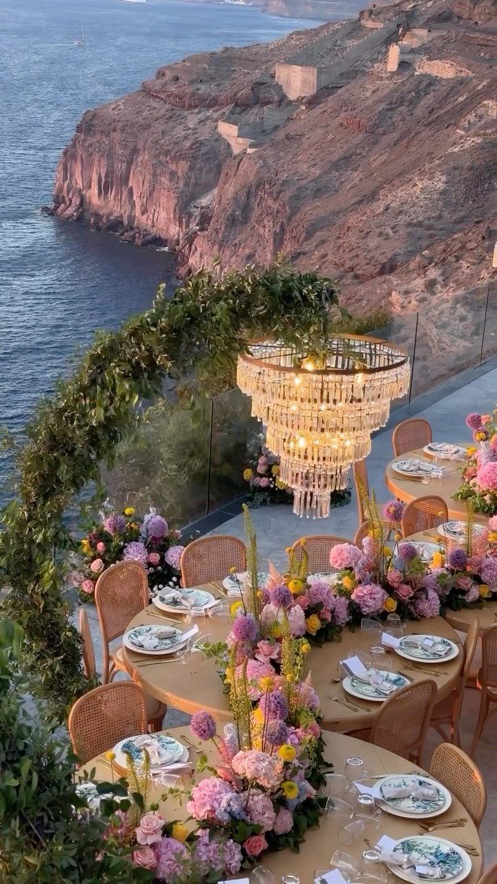 16 Marriage Theme Ideas for 2026: From Beach Ceremonies to Pearl Aesthetics 15 Wedding reception tables with floral arrangements and a crystal chandelier overlooking a coastal cliffside at sunset.
