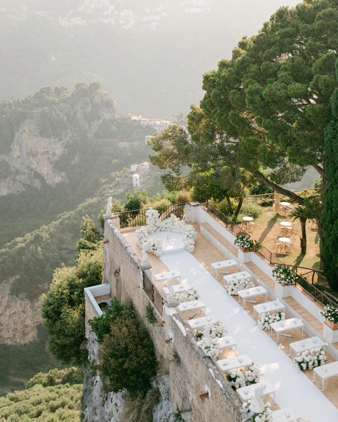 16 Marriage Theme Ideas for 2026: From Beach Ceremonies to Pearl Aesthetics 10 White wedding ceremony chairs and floral arrangements on a terrace overlooking a misty mountain landscape.