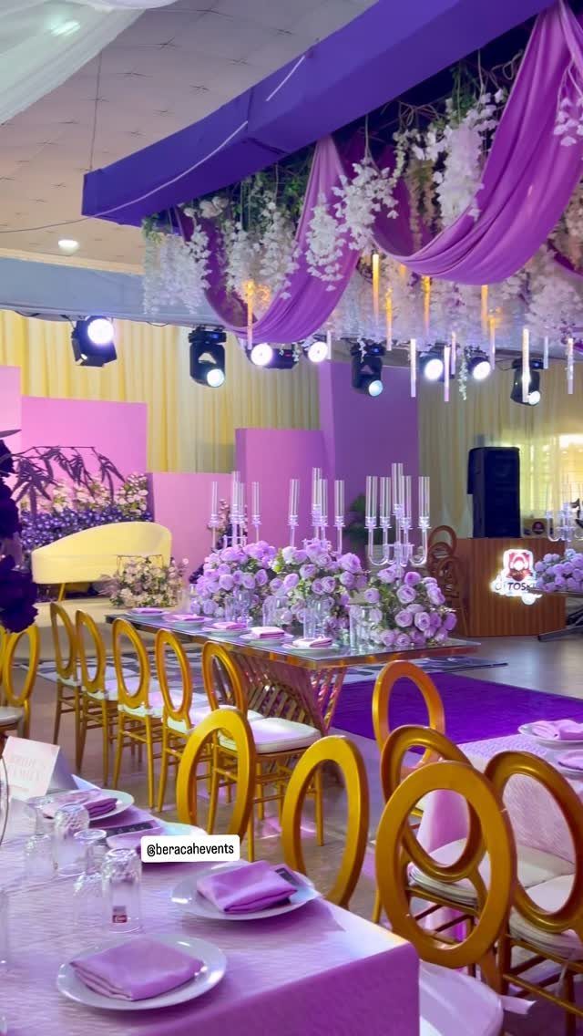 16 Marriage Theme Ideas for 2026: From Beach Ceremonies to Pearl Aesthetics 13 An indoor event space decorated with purple drapes, white floral arrangements, and elegant banquet table settings.