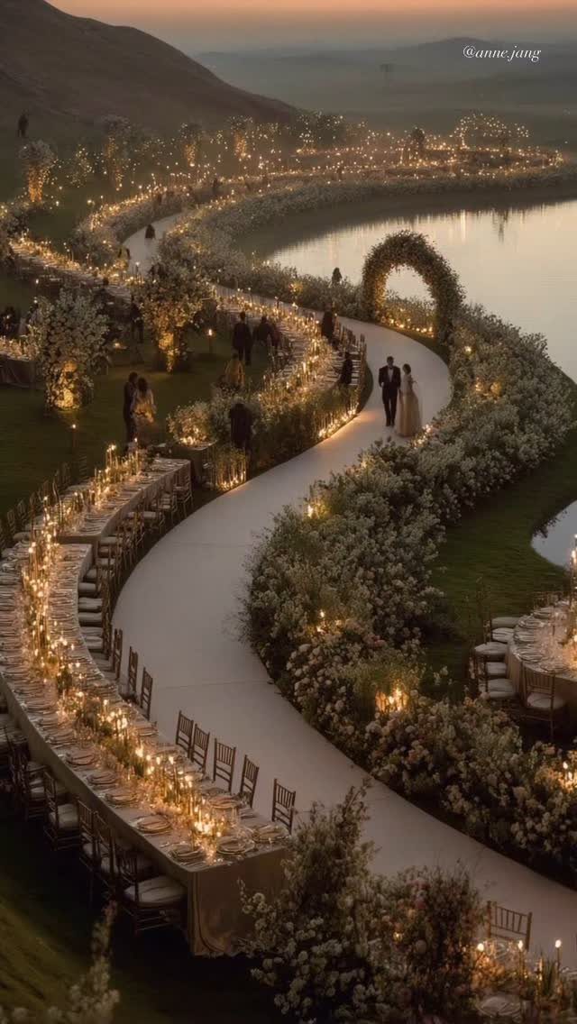 16 Marriage Theme Ideas for 2026: From Beach Ceremonies to Pearl Aesthetics 14 Aerial view of a winding outdoor wedding path decorated with white flowers and glowing candles by a lake.