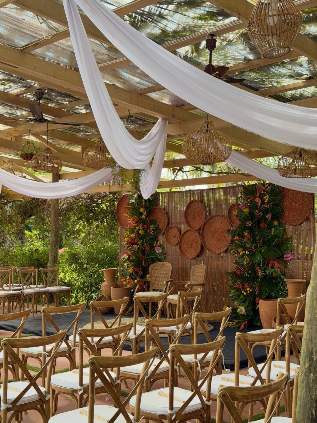 16 Marriage Theme Ideas for 2026: From Beach Ceremonies to Pearl Aesthetics 11 Wooden chairs arranged for an outdoor wedding ceremony under white fabric draping and woven lights.
