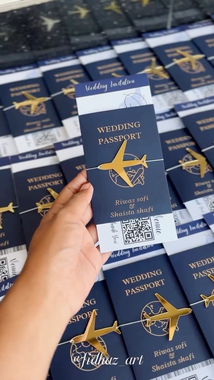 16 Marriage Theme Ideas for 2026: From Beach Ceremonies to Pearl Aesthetics 12 A hand holding a navy blue wedding passport invitation with gold airplane and text details.