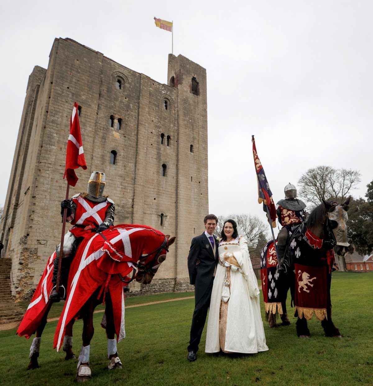 Medieval Wedding Theme: 7 Ideas for Your Day 6 A couple stands between two armored knights on horseback in front of a medieval stone castle.