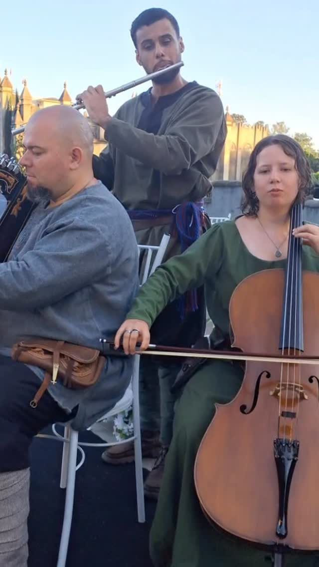 Medieval Wedding Theme: 7 Ideas for Your Day 4 Three musicians in medieval attire playing a flute, harp, and cello outdoors during sunset.
