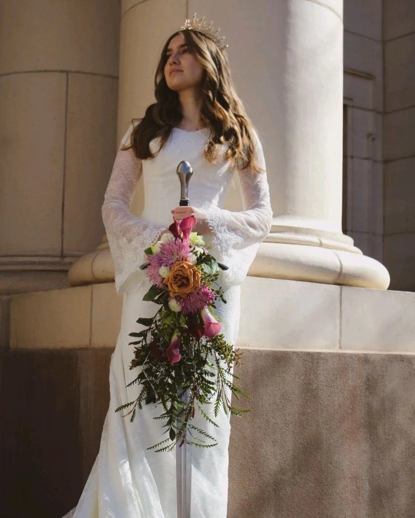 Medieval Wedding Theme: 7 Ideas for Your Day 2 A bride in a white lace gown holding a sword decorated with a floral bouquet.