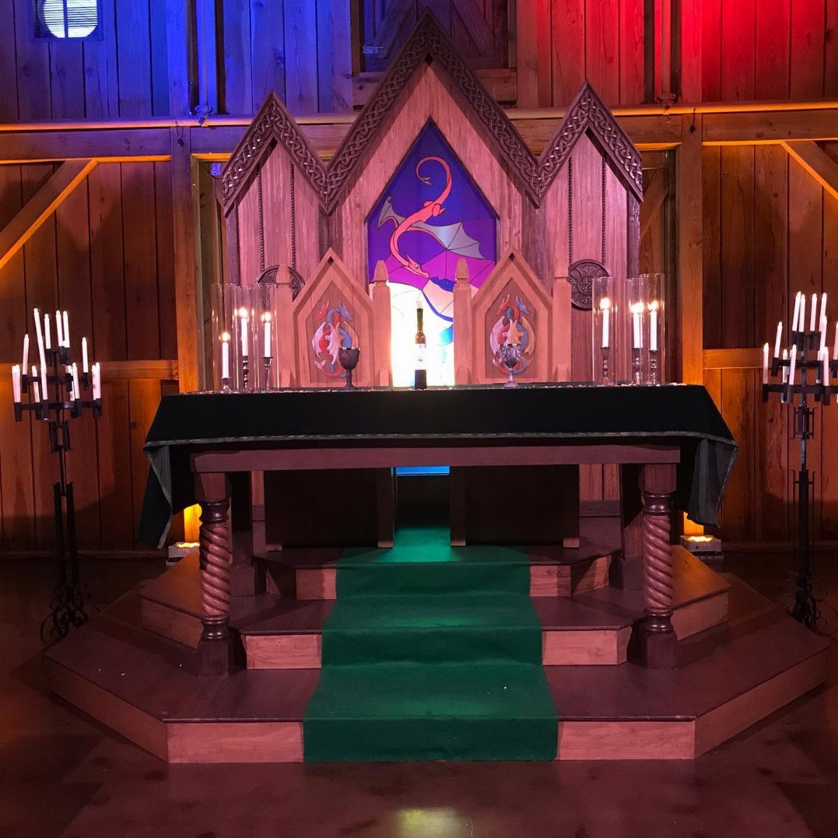 Medieval Wedding Theme: 7 Ideas for Your Day 5 Wooden altar with a dragon emblem backdrop, green tablecloth, and lit candles in a dimly lit room.