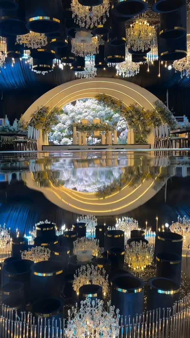 16 Navy Blue Wedding Theme Ideas for Every Part of Your Day 11 Crystal chandeliers hanging from a navy blue ceiling above a reflective floor and golden arch.