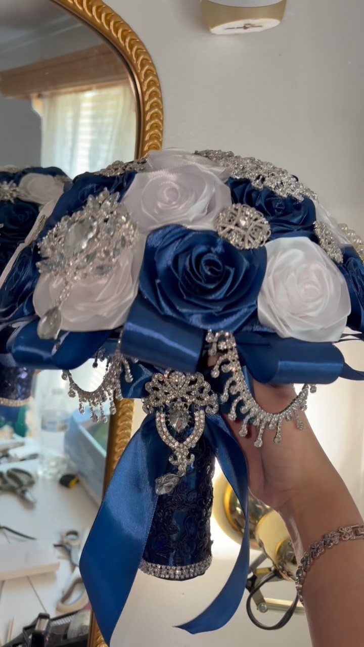 16 Navy Blue Wedding Theme Ideas for Every Part of Your Day 14 A hand holding a navy blue and white satin rose bouquet decorated with silver rhinestones.