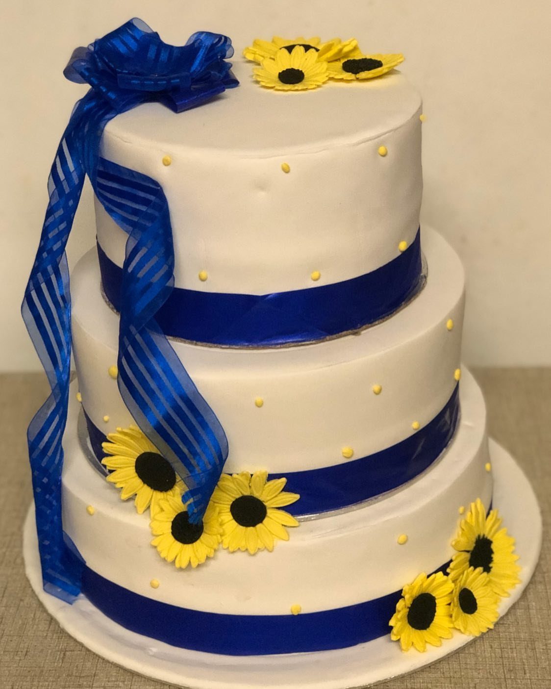 16 Navy Blue Wedding Theme Ideas for Every Part of Your Day 9 Three-tiered white wedding cake decorated with navy blue ribbons and bright yellow sunflowers.