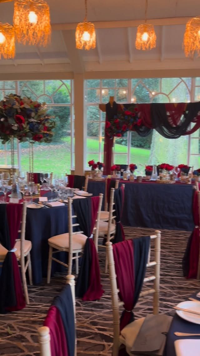 16 Navy Blue Wedding Theme Ideas for Every Part of Your Day 16 Wedding reception tables with navy blue cloths and burgundy chair sashes under warm hanging lights.