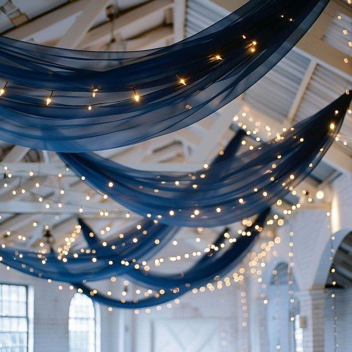 16 Navy Blue Wedding Theme Ideas for Every Part of Your Day 13 Navy blue fabric swags with warm fairy lights draped across a white ceiling.