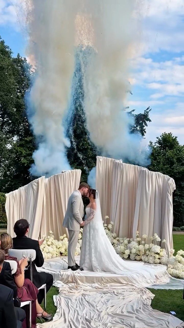 A bride and groom kissing in front of a dramatic draped backdrop and rising smoke.