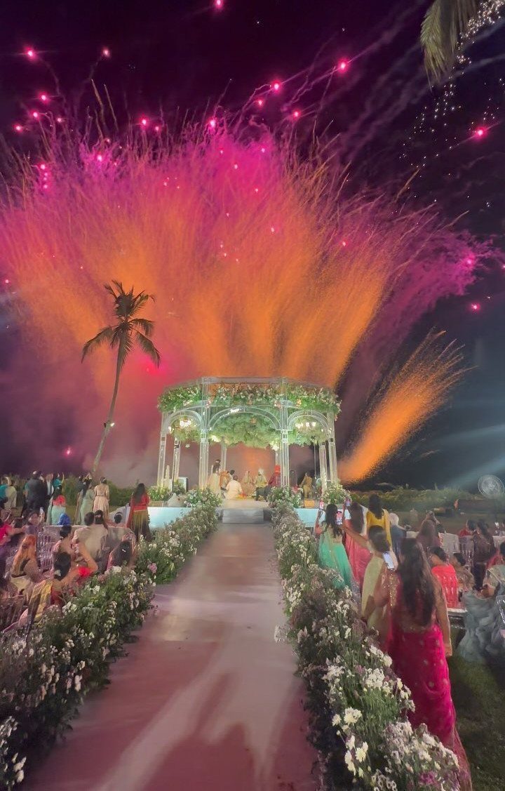 Fireworks exploding over a wedding ceremony with a floral gazebo and guests seated outdoors.