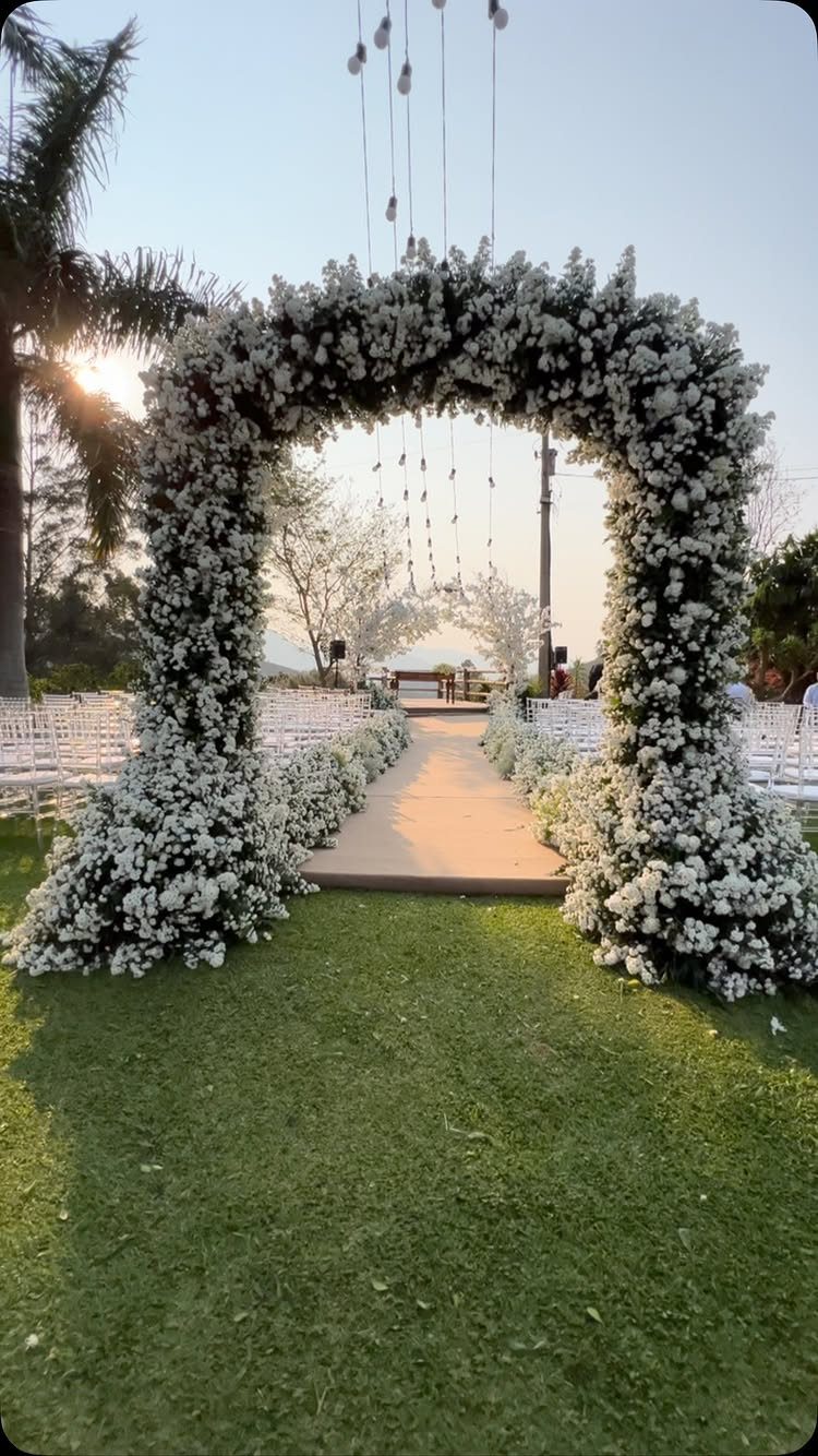 A white floral archway framing a grassy aisle with white chairs for an outdoor wedding ceremony.