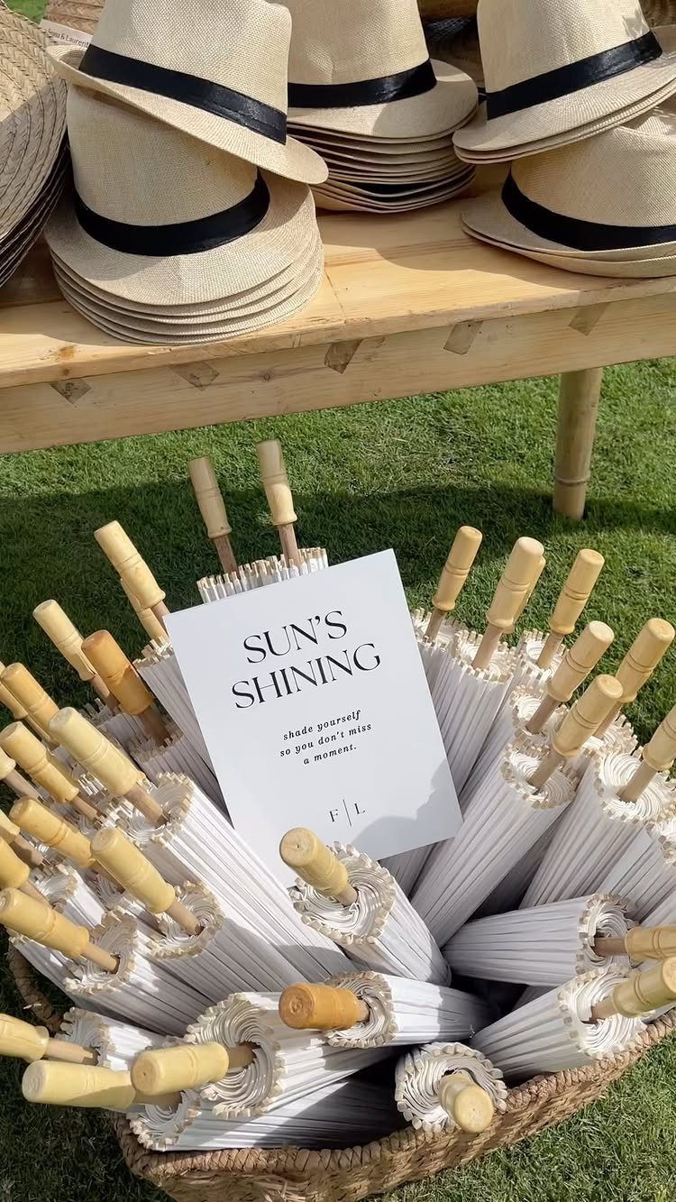 White parasols in a basket and straw hats on a wooden table outdoors.