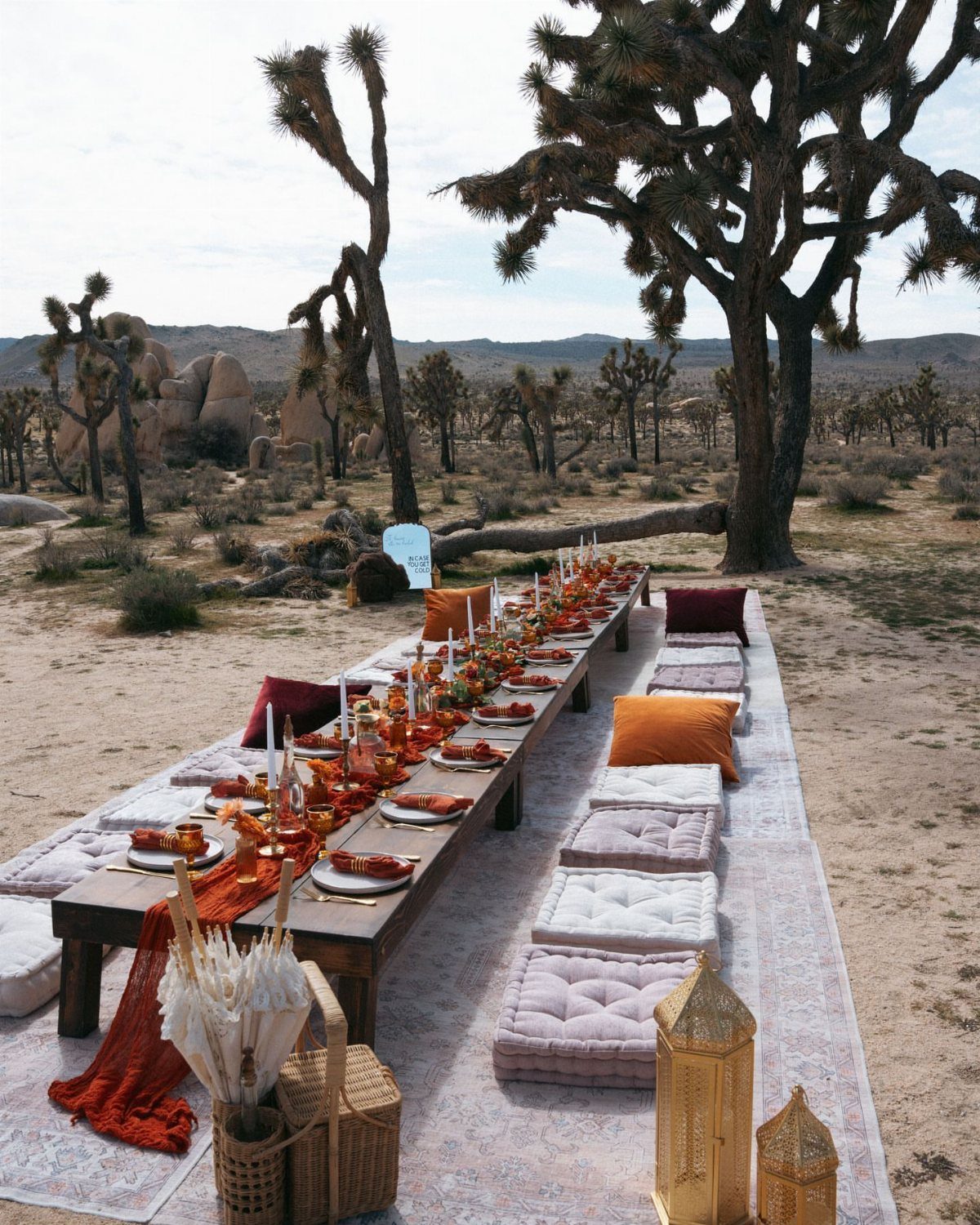 A long wooden dining table set with orange linens in a desert landscape.