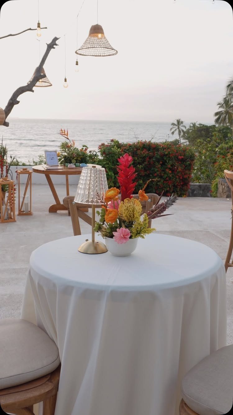 A white table with tropical floral centerpieces overlooking the ocean at sunset.