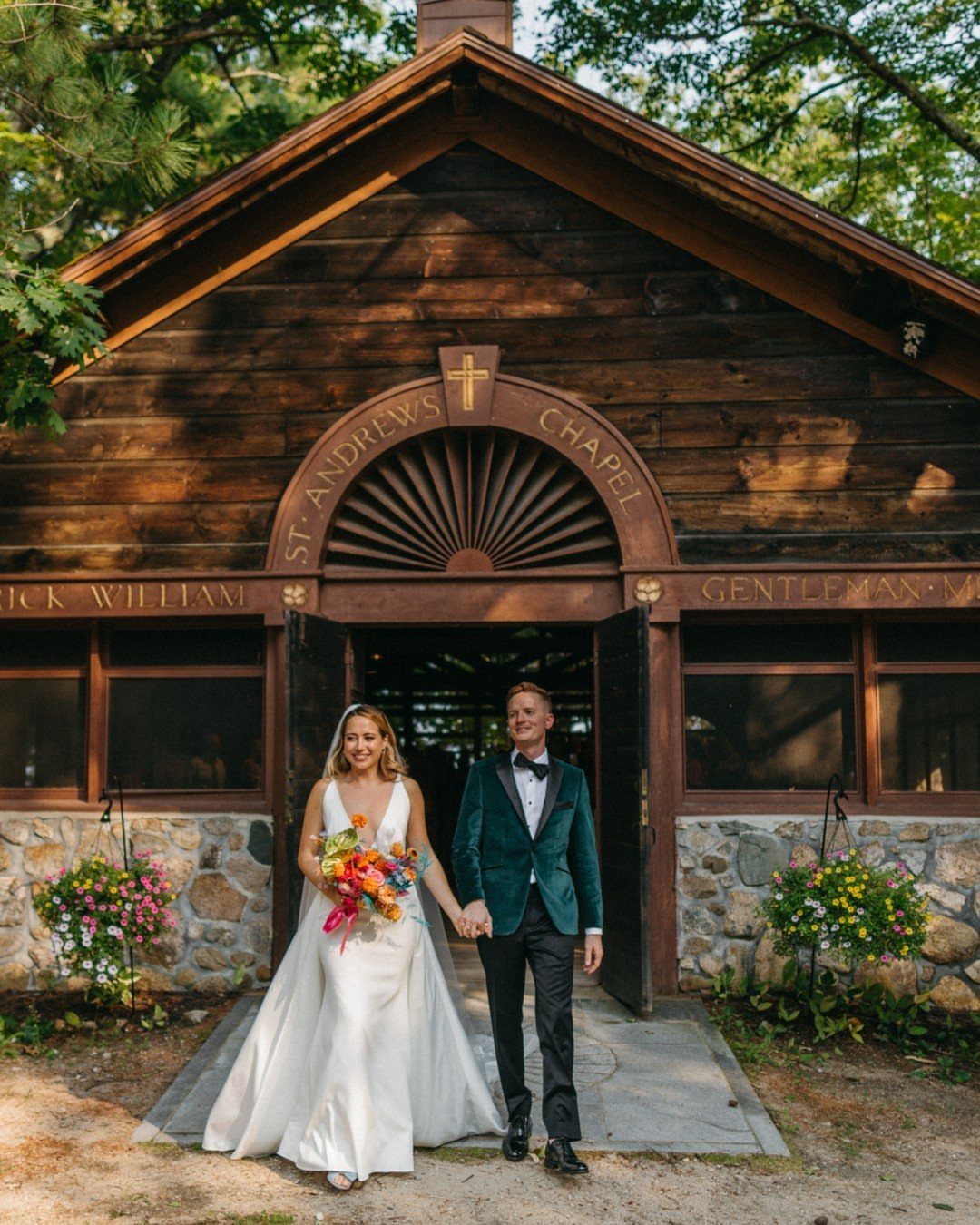 Bride and groom walking hand-in-hand in front of a rustic wooden chapel entrance.
