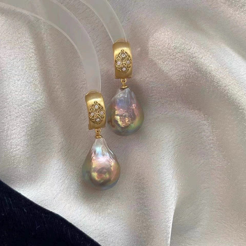6 Pearl Drop Earrings Bridal Looks for Your Wedding Day 3 Gold baroque pearl drop earrings resting on white satin fabric.