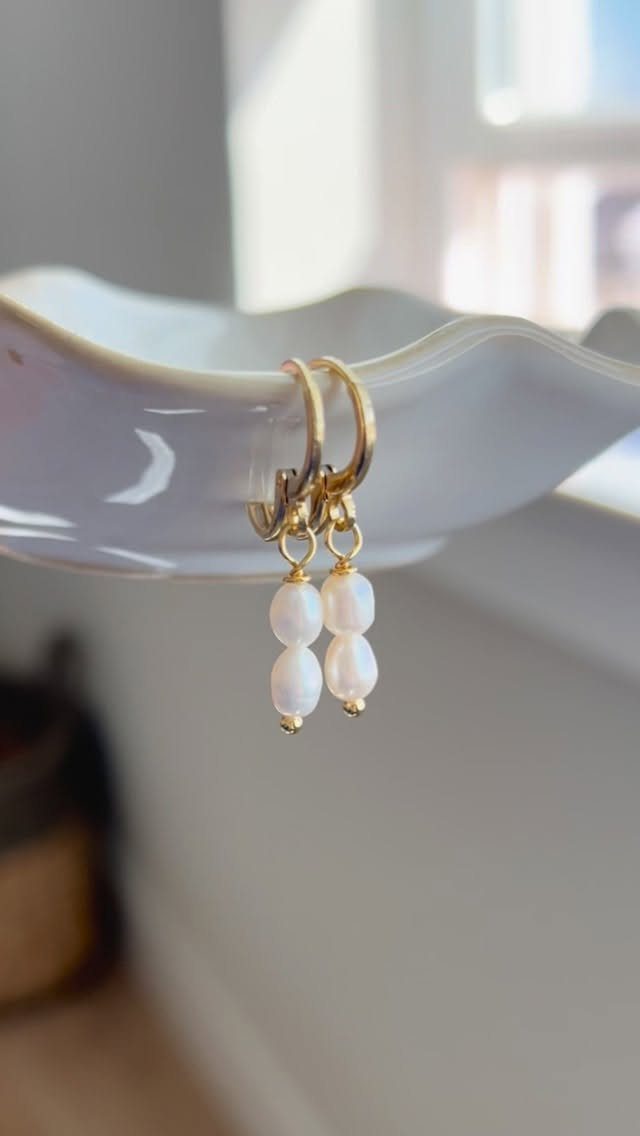 6 Pearl Drop Earrings Bridal Looks for Your Wedding Day 1 Gold hoop earrings with two graduated white pearls hanging from a white ceramic dish edge.