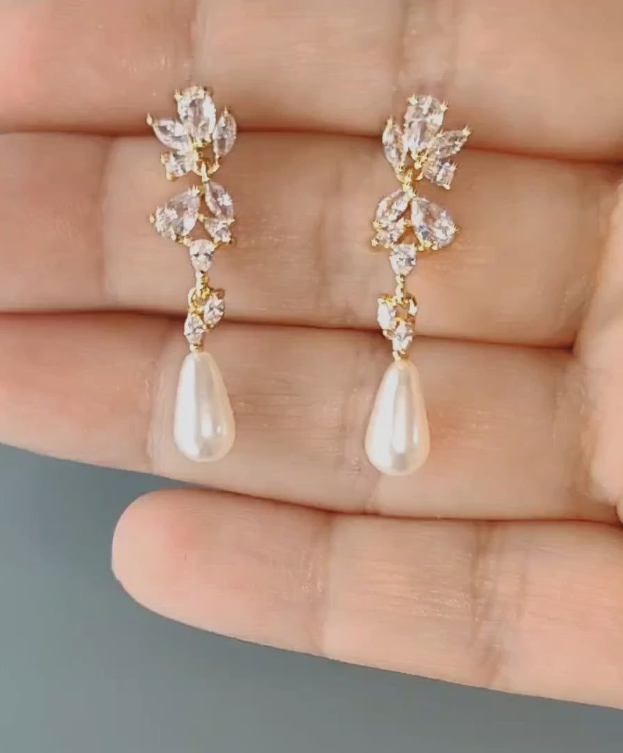6 Pearl Drop Earrings Bridal Looks for Your Wedding Day 4 Gold-tone earrings with clear stones and large teardrop pearls held in a person's hand.