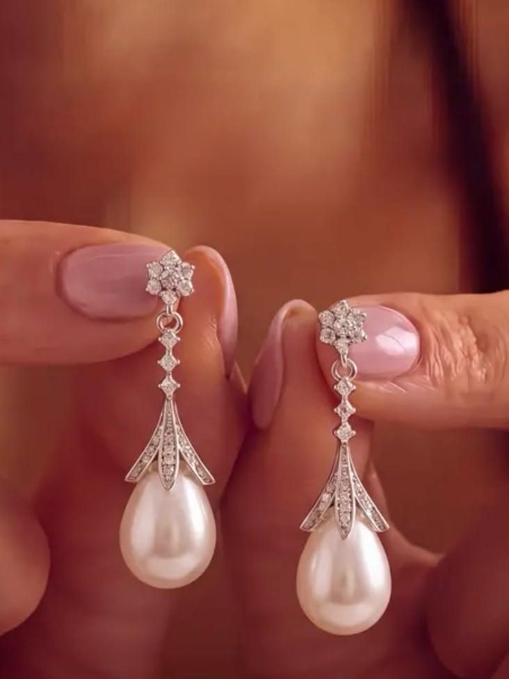 6 Pearl Drop Earrings Bridal Looks for Your Wedding Day 5 Silver-toned teardrop earrings with large white pearls held between two fingers with pink manicured nails.