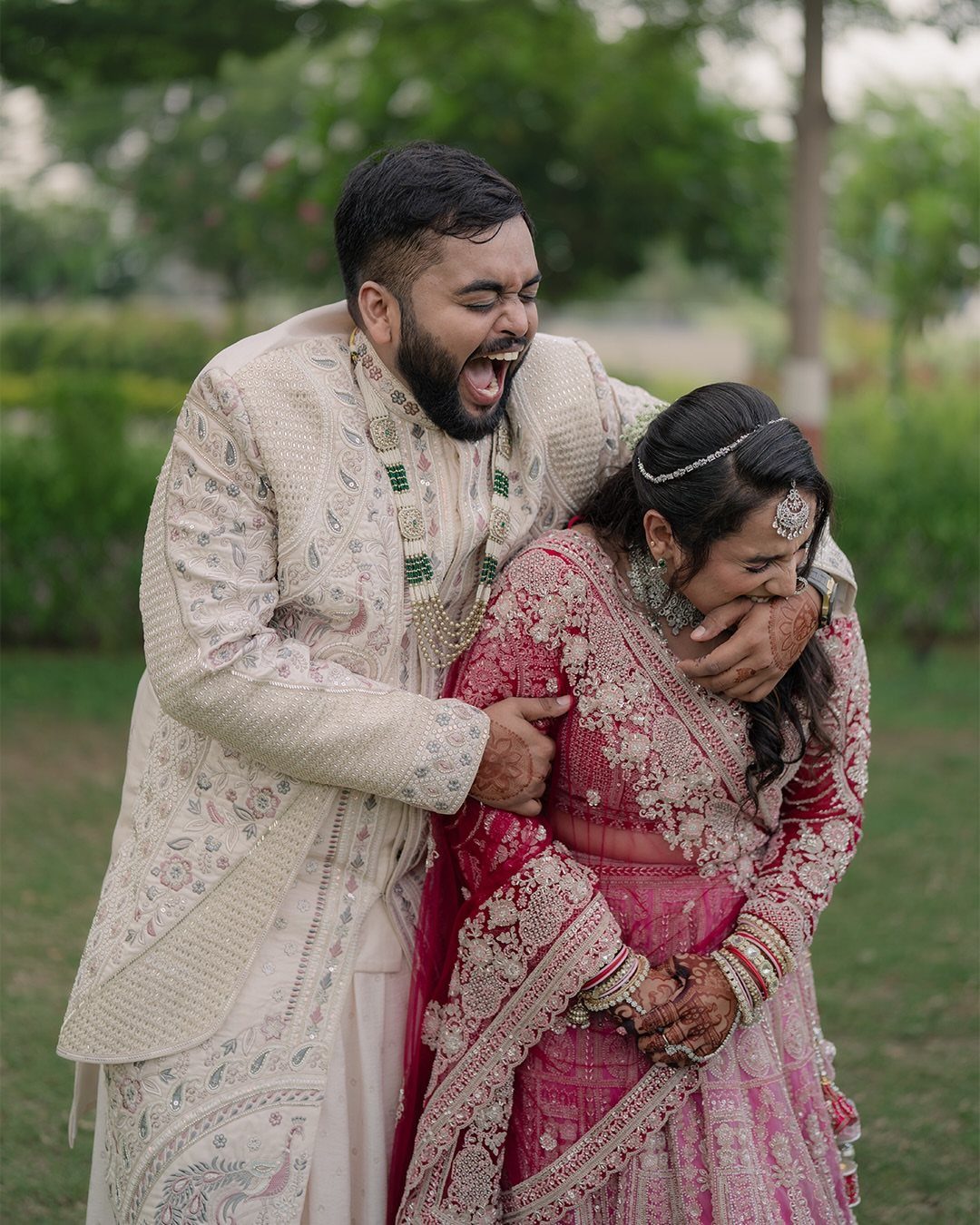 19 Photosession Ideas for Your Wedding Ceremony 18 A laughing man in cream traditional attire and a woman in pink lehenga sharing a joyful moment outdoors.