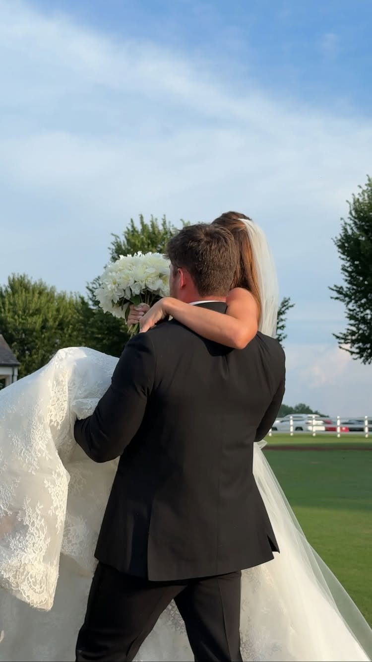19 Photosession Ideas for Your Wedding Ceremony 13 A groom in a black suit carries his bride in a white lace gown outdoors.