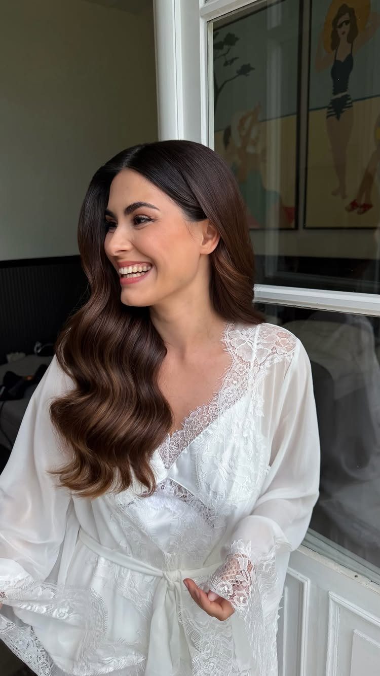19 Photosession Ideas for Your Wedding Ceremony 17 A smiling woman with wavy brown hair and elegant makeup wearing a white lace robe.