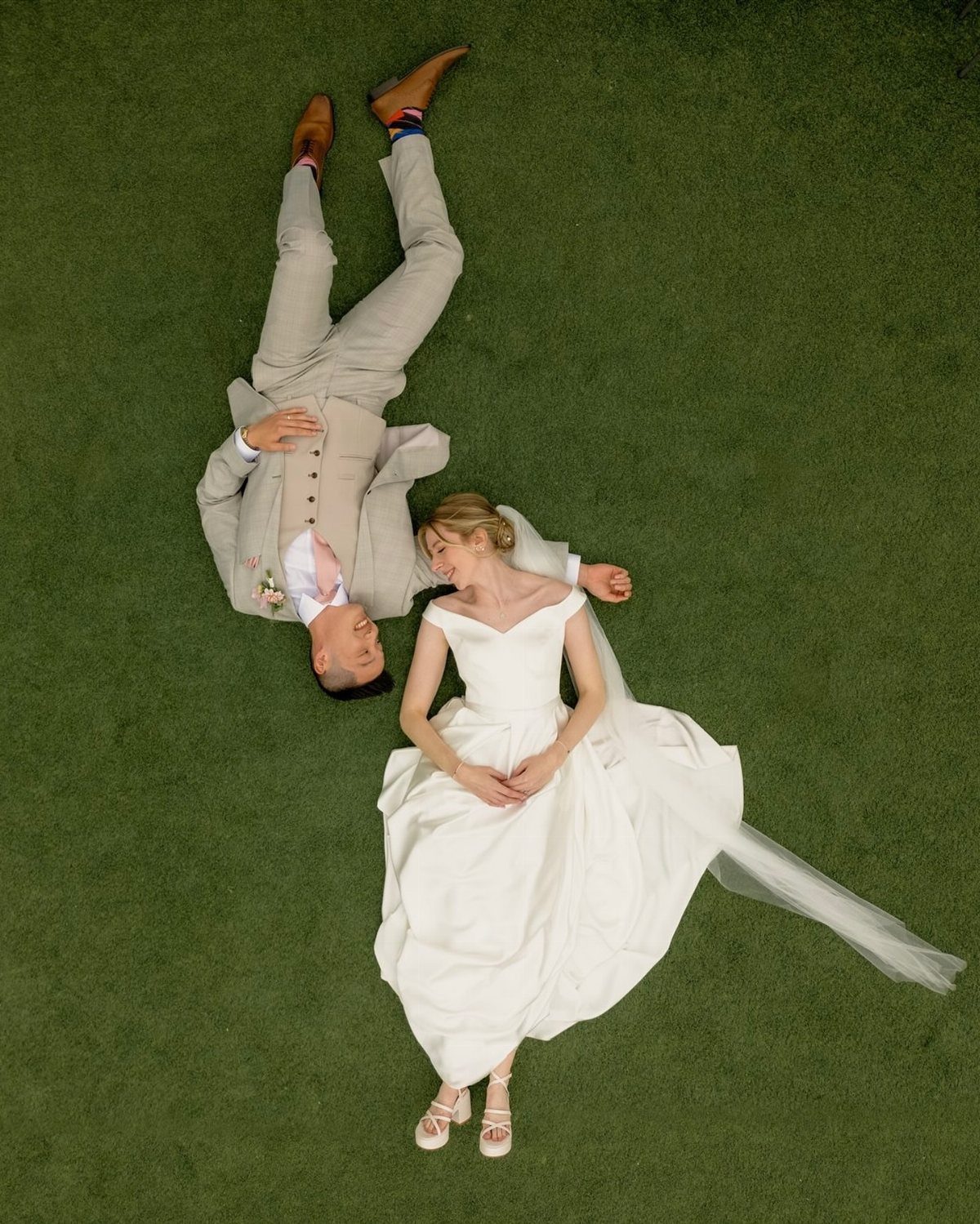19 Photosession Ideas for Your Wedding Ceremony 14 A bride and groom lying on green grass looking at each other from an aerial perspective.