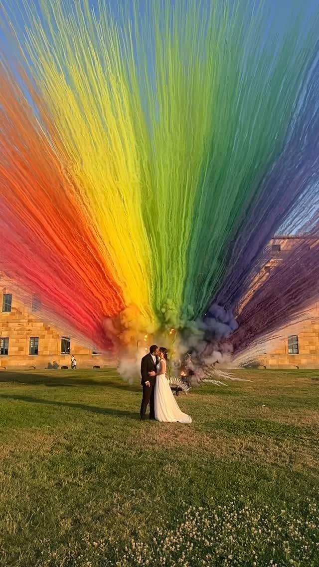 19 Photosession Ideas for Your Wedding Ceremony 9 A bride and groom stand before a massive, colorful rainbow smoke bomb explosion.
