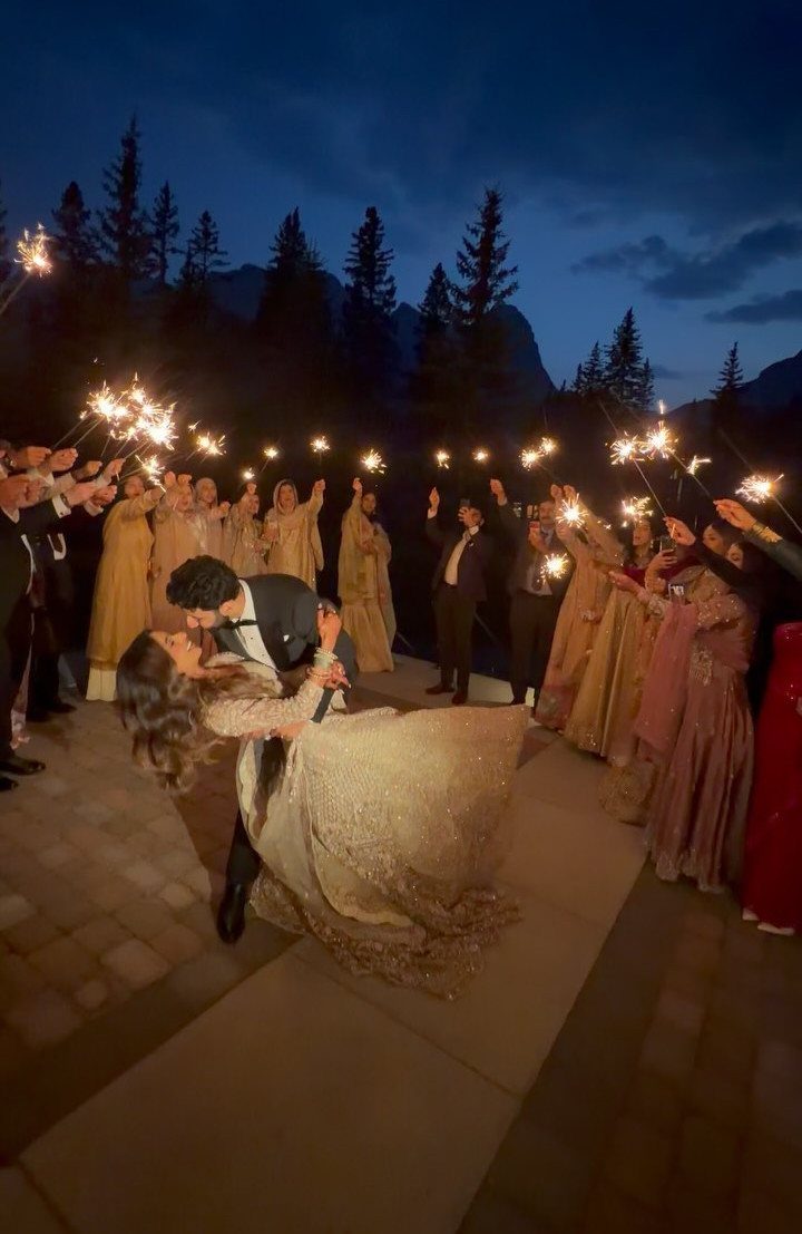 19 Photosession Ideas for Your Wedding Ceremony 11 A bride and groom kissing surrounded by wedding guests holding glowing sparklers at night.