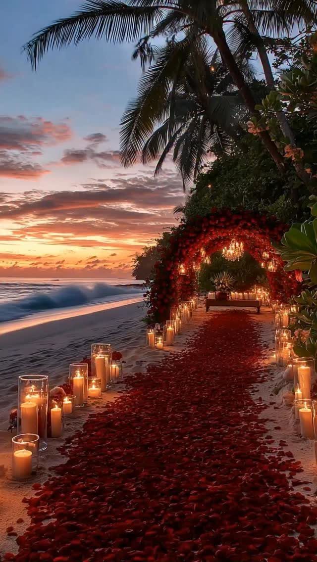 12 Romance Wedding Theme Ideas That Actually Feel Personal 1 Red rose petals form a path on a beach lined with glowing candles at sunset.