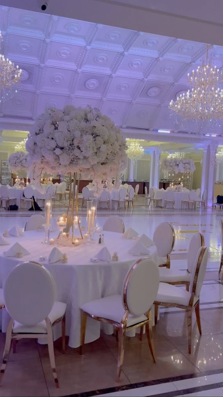 12 Romance Wedding Theme Ideas That Actually Feel Personal 2 Large white floral tower centerpiece on a round wedding table with gold-framed chairs.