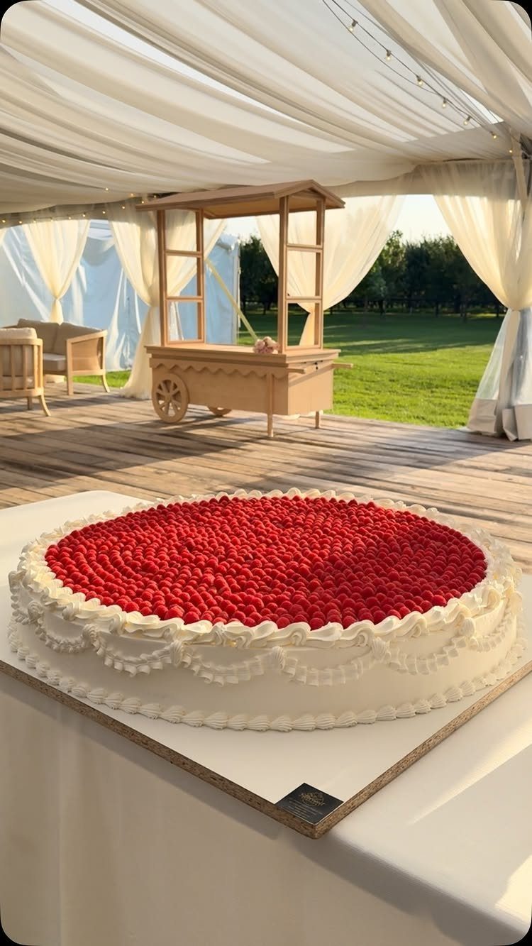 12 Romance Wedding Theme Ideas That Actually Feel Personal 6 Large white frosted cake covered in bright red berries on a table under a white tent.