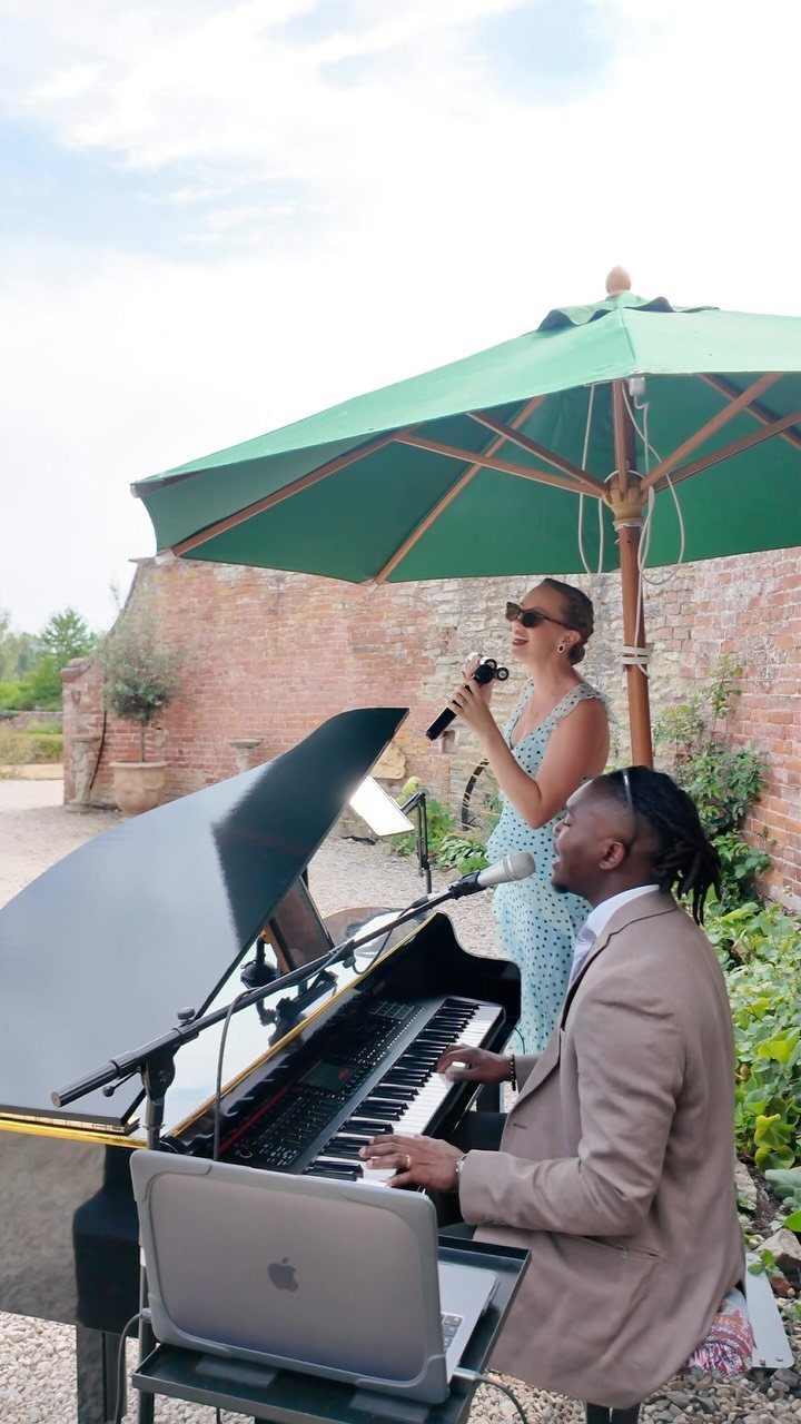 12 Romance Wedding Theme Ideas That Actually Feel Personal 4 A woman singing into a microphone while a man plays a black grand piano outdoors.