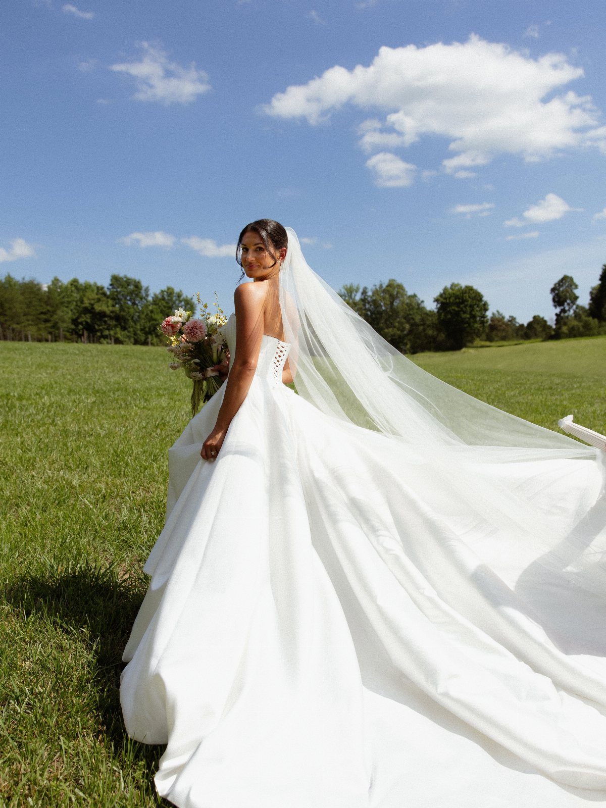 12 Romance Wedding Theme Ideas That Actually Feel Personal 9 A bride in a white wedding dress and long veil stands in a grassy field.
