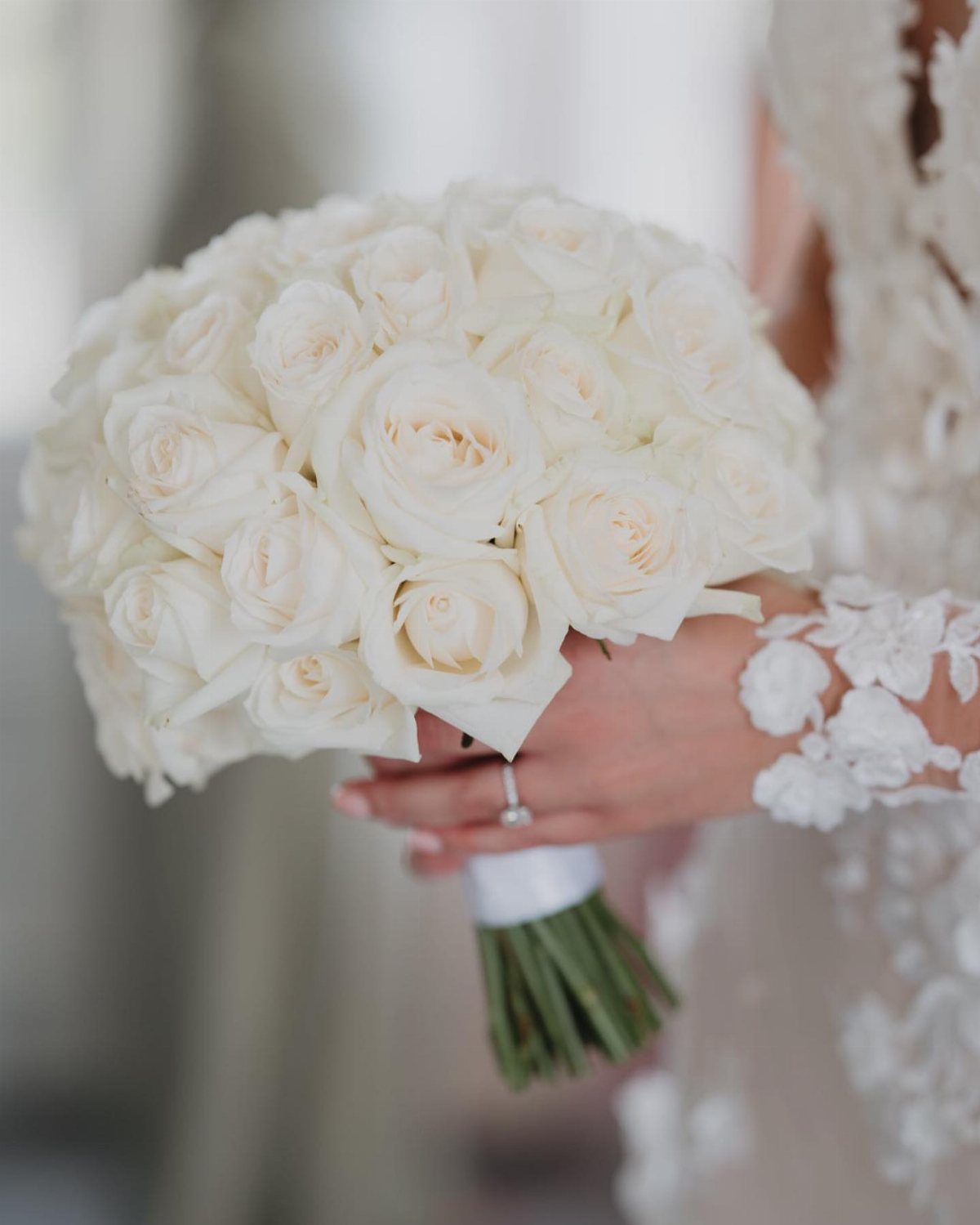 A bride holding a lush bouquet of white roses wrapped in white ribbon.