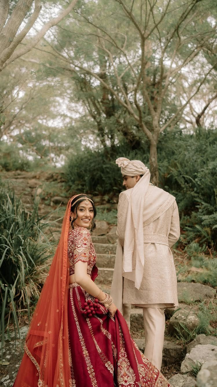 A bride in red and a groom in cream walking up stone steps in a forest.