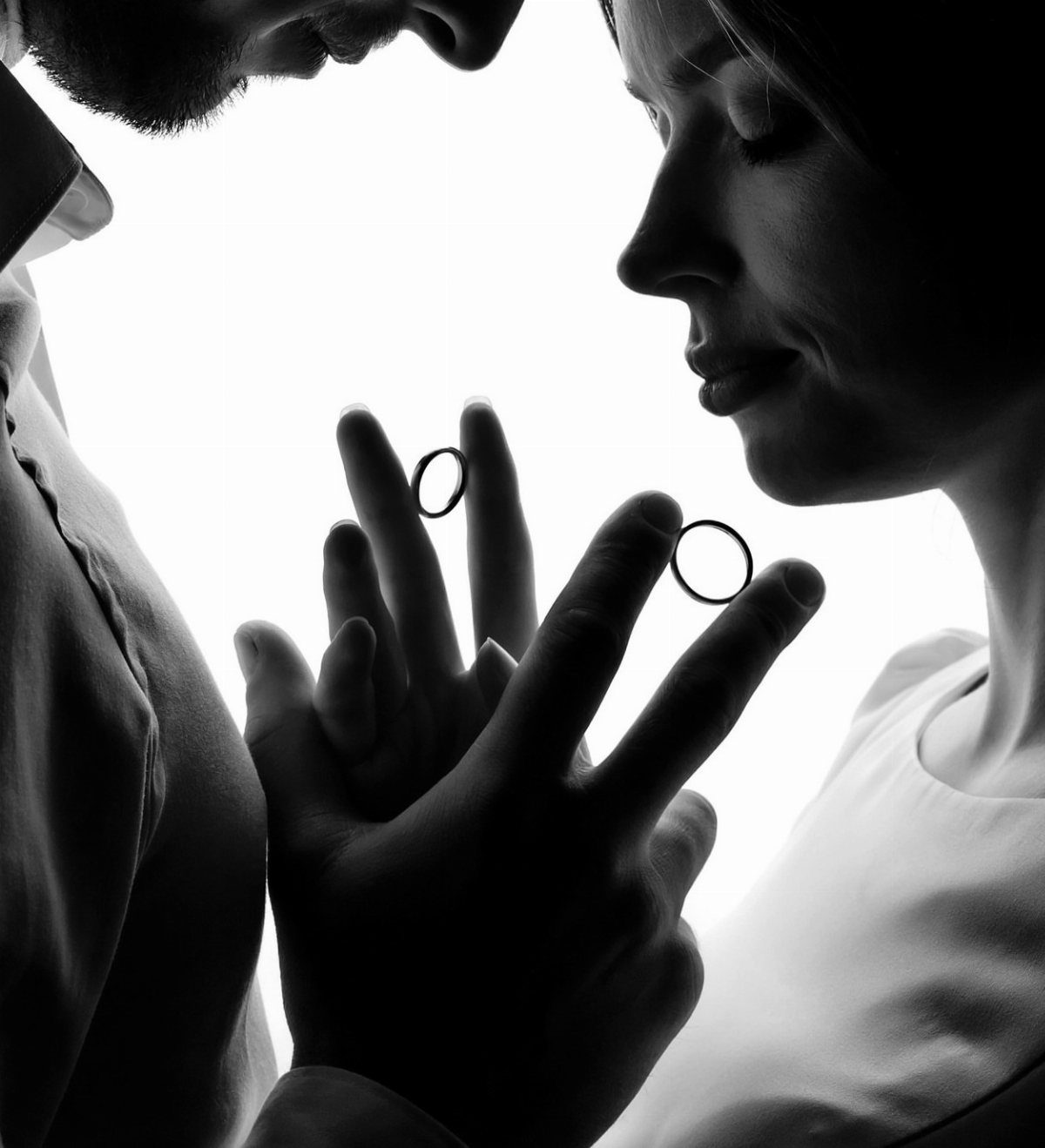 Silhouette of a man and woman holding wedding rings between their intertwined hands.