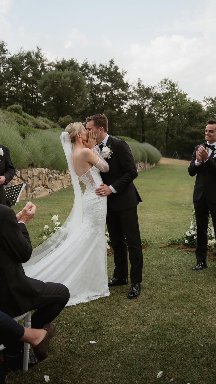 A bride and groom leaning in to kiss during an outdoor wedding ceremony on a lawn.