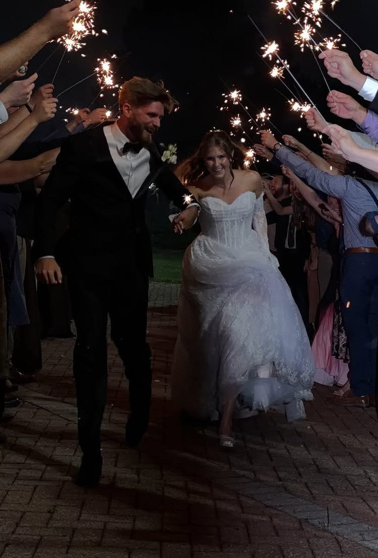 A bride and groom walking through a tunnel of guests holding glowing sparklers at night.