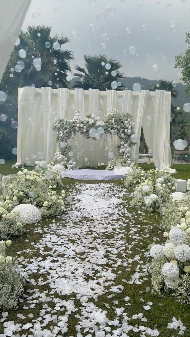 White flower petals scattered on grass leading to a white rug and floral wedding ceremony arch.