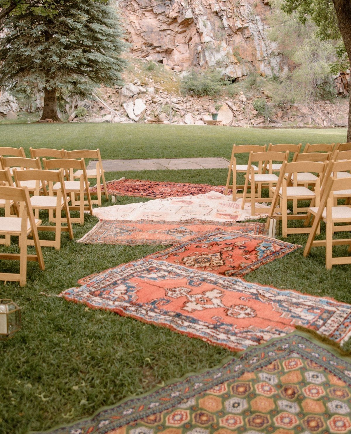 Colorful patterned vintage rugs laid out on grass to form a wedding ceremony aisle.